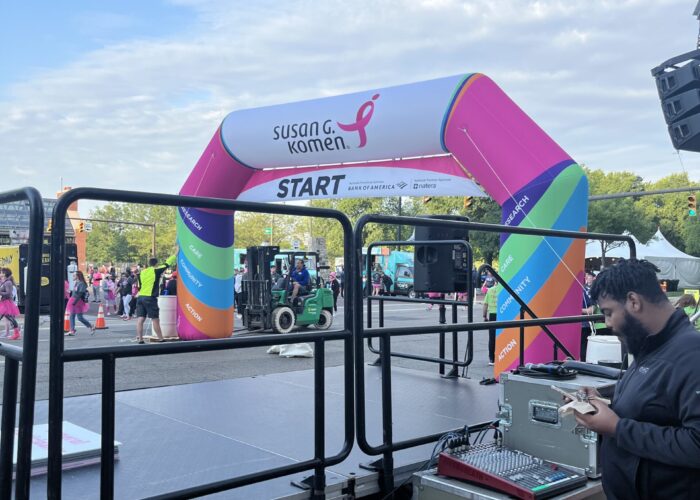 Colorful race start arch labeled 'Susan G. Komen' with 'START' text, crowd and event tents in the background.